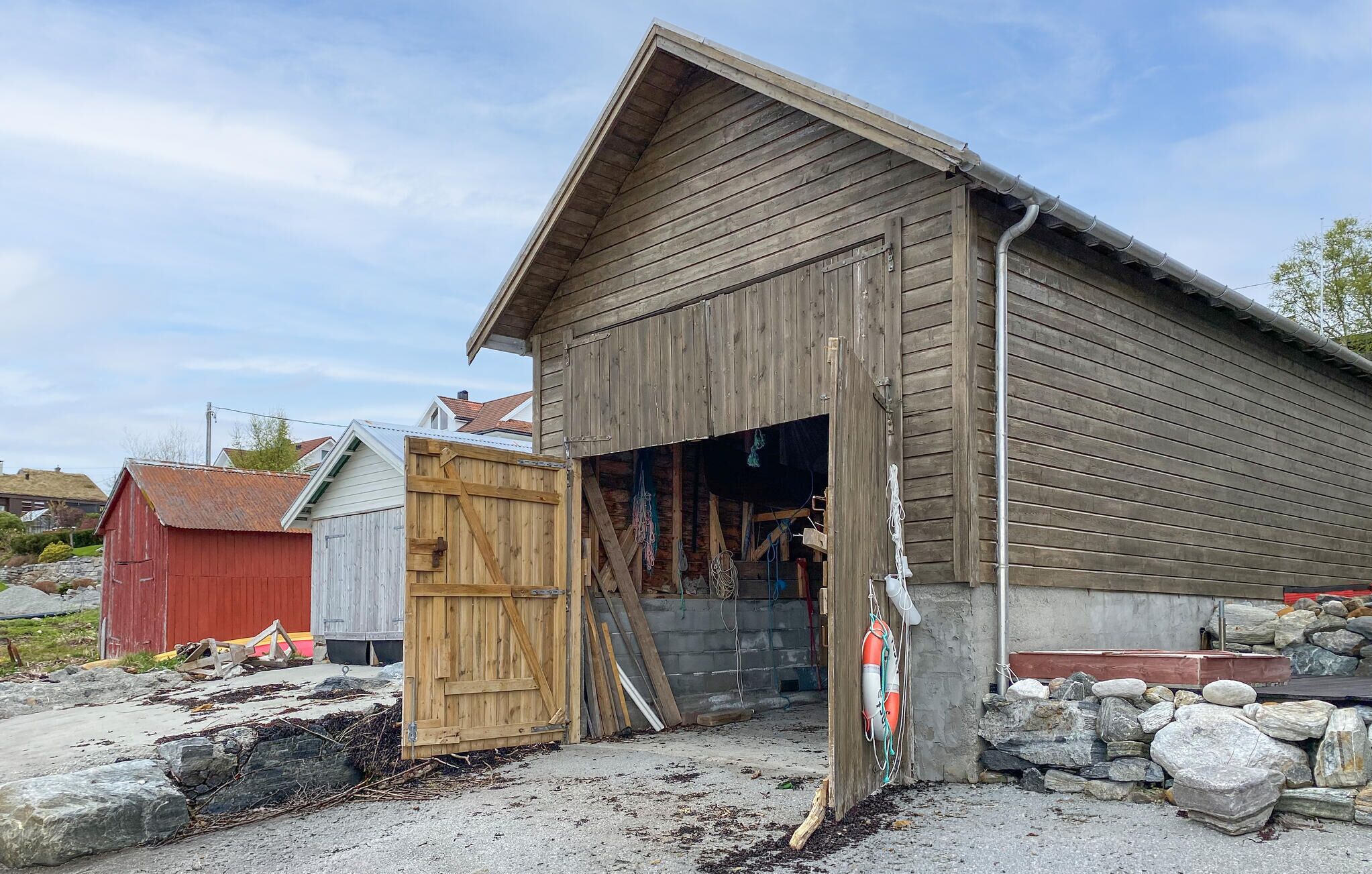 Un edificio de madera con un amplio portón abierto, un cobertizo rojo y materiales de construcción en el exterior.