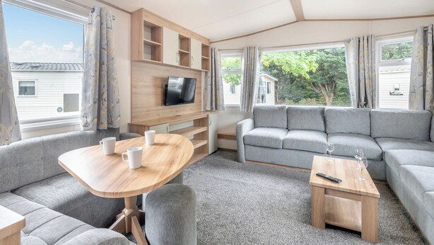 Ein modernes Wohnmobil-Interieur mit einer Sitzecke, Tisch, Fernseher und Stauraumregalen.