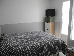 A bedroom with a bed, a TV on a stand, a window, and a door. - House 5 mn walk from the center of aiguillon (L'Aiguillon-la-Presqu'île)