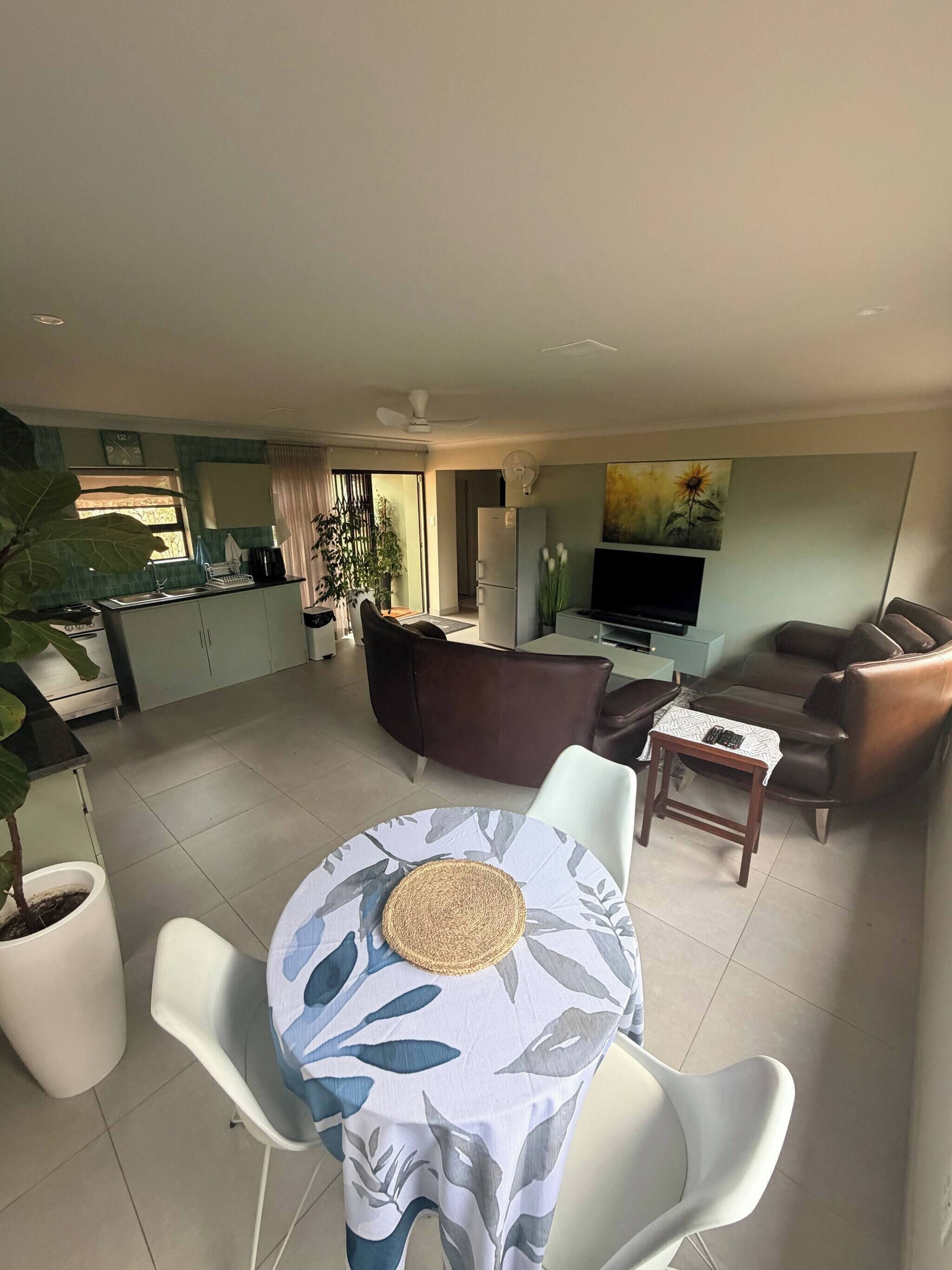A modern living room with a dining area, a flat-screen TV, and a ceiling fan.
