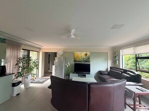 A modern living room with a sofa, a TV, a fan, and a painting of a sunflower. - Kalistas Cottage Wilropark (Johannesburg)