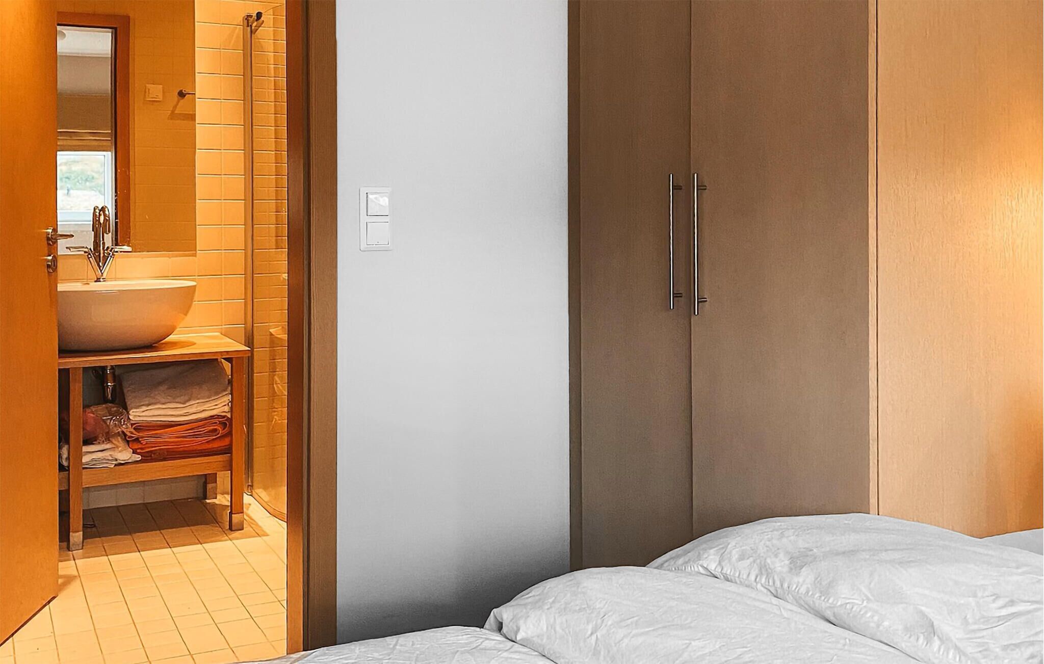 A bedroom with a bed, a wooden wardrobe, and a bathroom with a sink and towel rack.