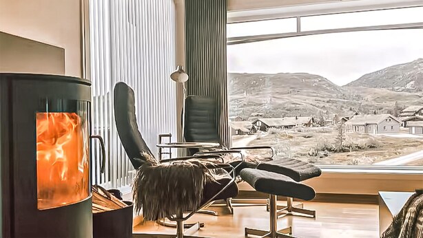 Een moderne woonkamer met een open haard, een comfortabele fauteuil, een tafel en een groot raam met uitzicht op het buitengebied.