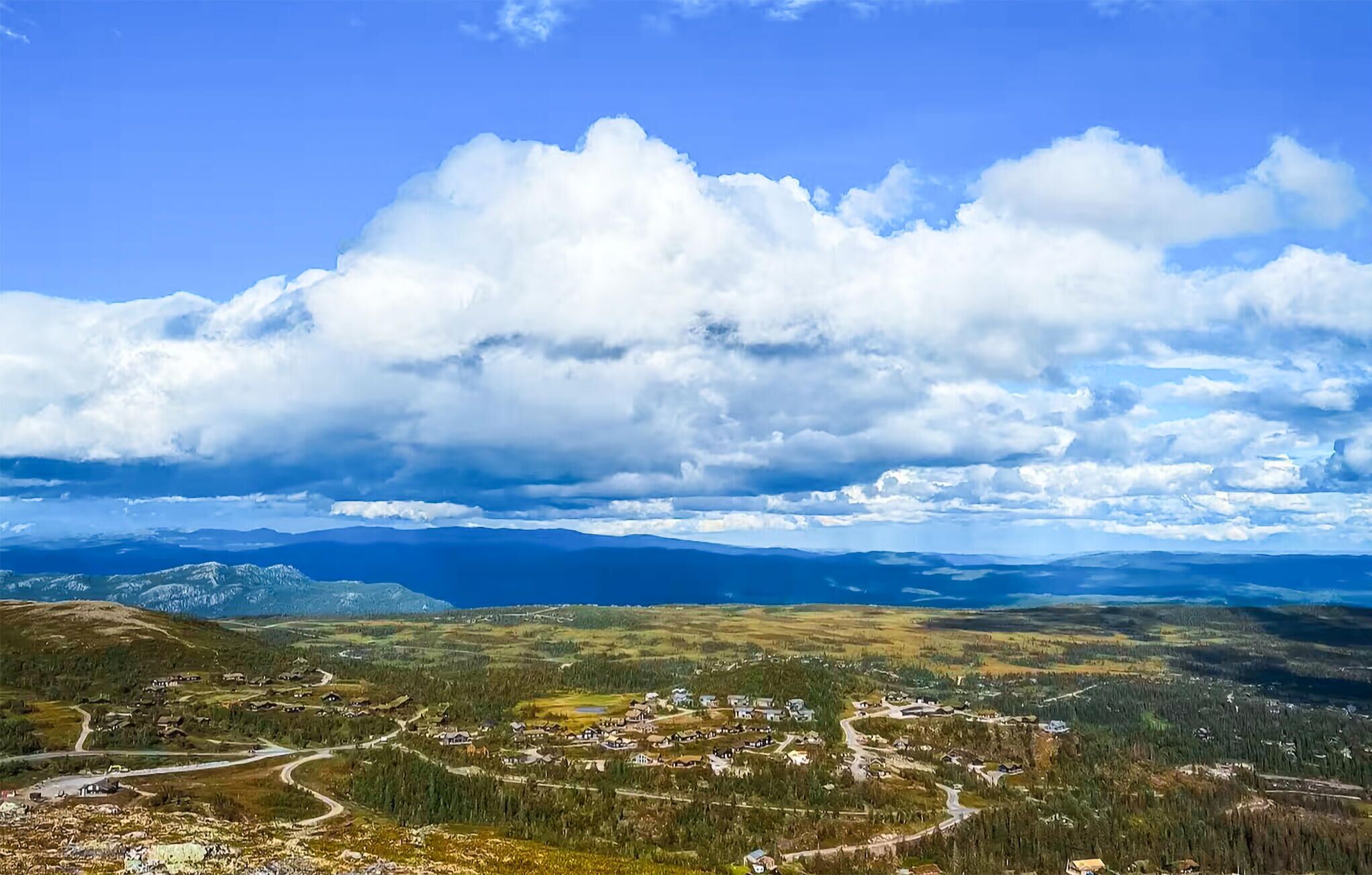 Une vue panoramique d’un paysage montagneux, avec un petit village et une route sinueuse.