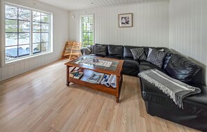 A living room with a black leather sofa, a wooden coffee table, and a view through large windows. - Amazing home in ørje with WiFi (Ørje)