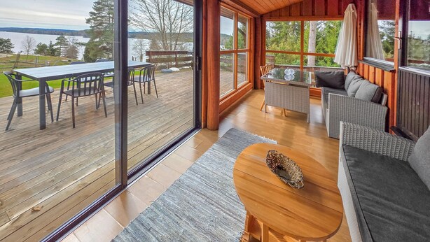A spacious deck with a dining area, a seating area with a sofa and chairs, and large windows offering a view of the outdoors. - Amazing home in ørje with house sea view (Ørje)