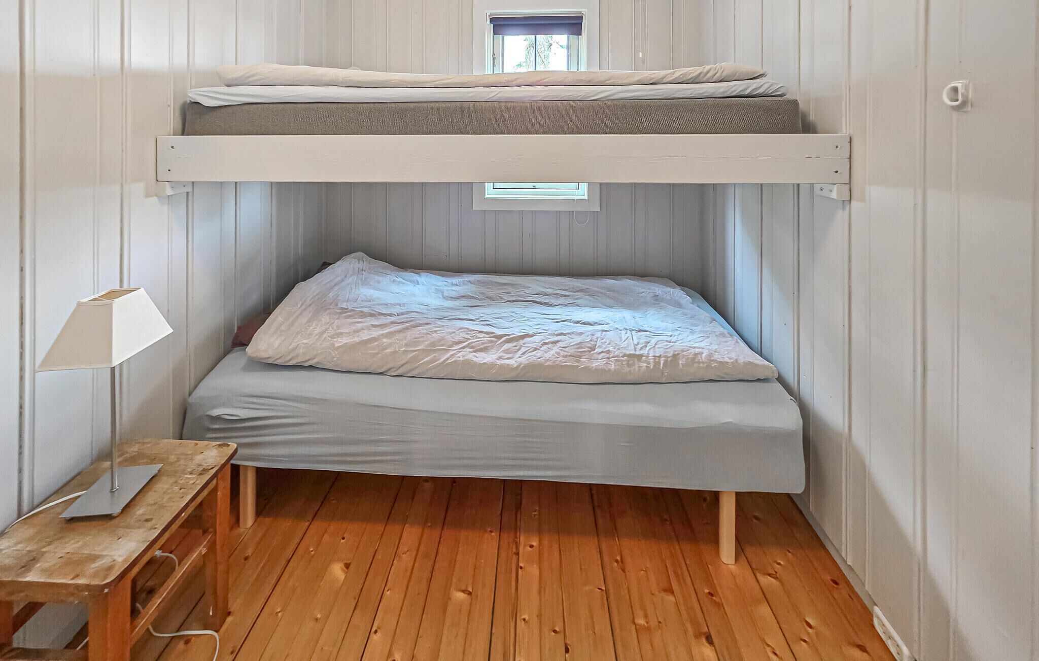 A bunk bed with a window above, a desk with a lamp, and wooden flooring.