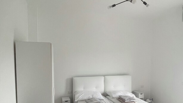 Ett minimalistiskt sovrum med en enkel säng, sängbord och en modern lampa.
