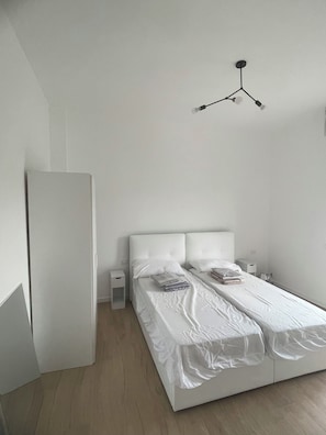 Une chambre à coucher minimaliste, avec un lit simple, des tables de chevet et un luminaire moderne.