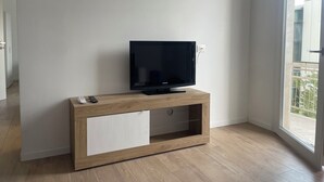 Ett modernt vardagsrum med en platt-TV på ett TV-bord i trä, en skjutdörr som leder ut till en balkong och en vägg i en ljus färg.
