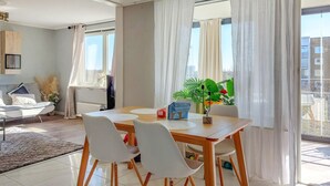 Moderni olohuone, jossa on ruokapöytä, valkoiset tuolit, sohva ja suuri ikkuna, jossa on verhot.