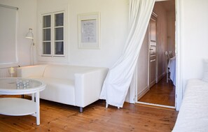 A room with a white sofa, a small round table with candles, a framed menu on the wall, and a door leading to a dining area. - 4 bedroom nice home in Trelleborg (Trelleborg)