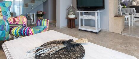 Ett vardagsrum med en tv, färgglada stolar, ett vitt soffbord och en trappa.