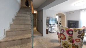 Eine Treppe führt zu einem Wohnbereich mit Fernseher, Kamin und einem bunten Sessel.
