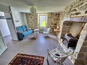 A living room with a stone wall, a fireplace, a sofa, a small table, and a patterned rug. - 734 – Seaside holiday home in Primelin, Brittany (Primelin)