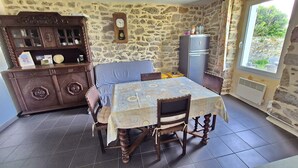 Un coin repas avec une table dressée pour deux personnes, un buffet en bois aux portes vitrées, un mur en pierre et une fenêtre offrant une vue agréable.