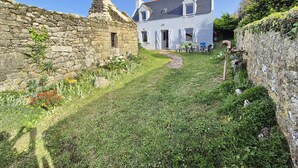 Un mur de pierre, un sentier bordé d’herbe et un bâtiment blanc avec un toit gris.