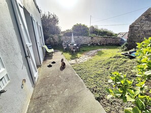 Un patio trasero con un camino de concreto, un perro pequeño, muebles de exterior y un muro de piedra.