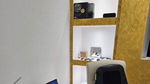 Despatx modern amb escriptori blanc, cadira d'oficina negra, un portàtil, un bol amb aperitius i una estant amb diversos objectes.