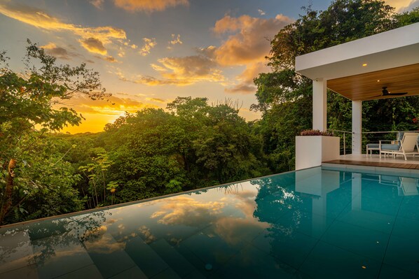 A modern outdoor pool with a clear view of the surrounding lush greenery and a sunset.