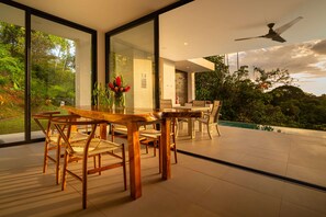 A modern dining area with a glass wall, wooden furniture, and a ceiling fan.
