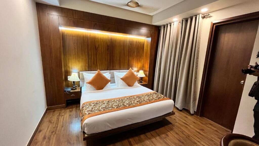 A hotel room with a large bed, wooden headboard, and a nightstand with lamps.