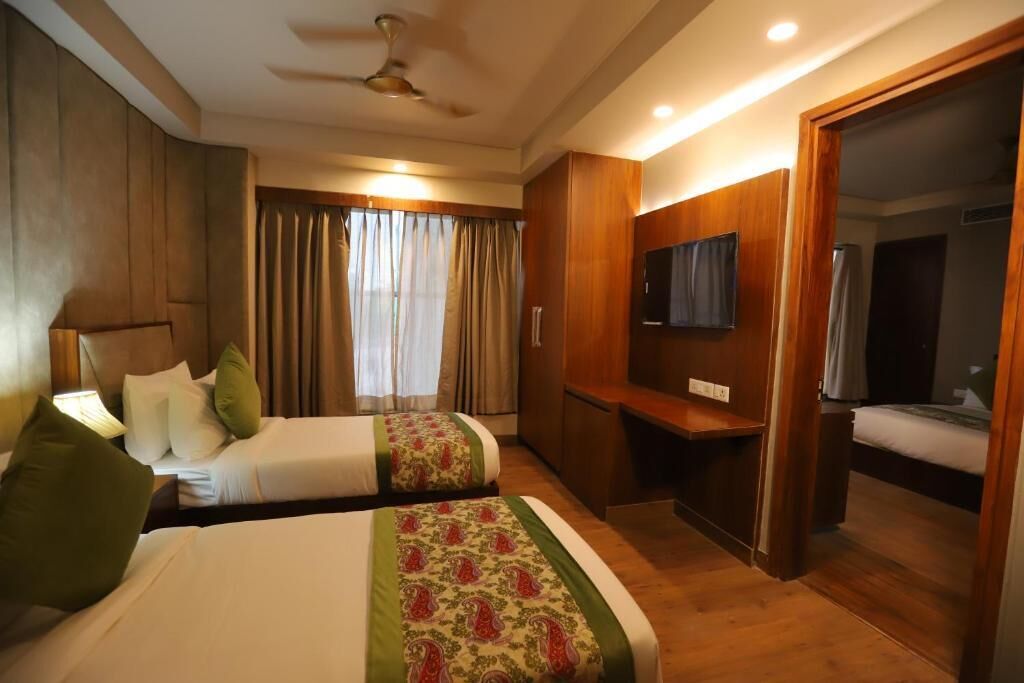 A hotel room with two beds, a desk, a television, and a mirror.