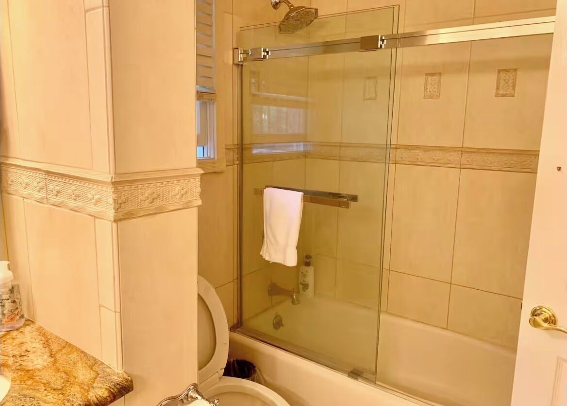 A bathroom with a glass-enclosed shower, a toilet, and a marble countertop.