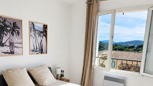Une chambre à coucher avec un lit, une table de chevet, une fenêtre donnant sur un beau paysage et deux tableaux encadrés accrochés au mur.