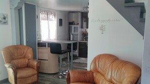 Un salon avec des fauteuils en cuir, une table basse en verre et un escalier menant à la cuisine.