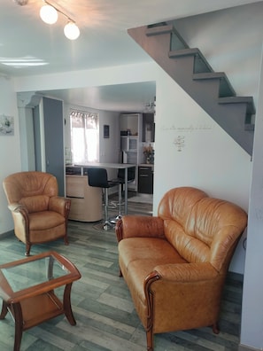 Ein Wohnzimmer mit Ledersesseln, einem Glastisch und einer Treppe, die zur Küche führt.