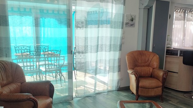 Une pièce avec une table en verre, deux fauteuils en cuir, un plancher en bois et une vue sur une piscine, visible à travers une porte vitrée.