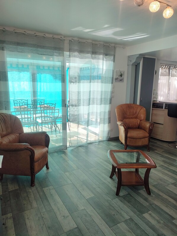 Ein Zimmer mit Glastisch, zwei Ledersesseln, Holzboden und Blick auf einen Pool durch eine Glastür.