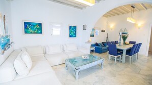Uma sala de estar ampla com um sofá branco, uma mesa de centro de vidro e uma área de jantar com mesa e cadeiras.