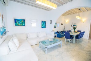 A spacious living area with a white sofa, a glass coffee table, a dining table with chairs, and artwork on the walls. - Mykonian style house ,3 min walk from Ornos Beach (Ornos)