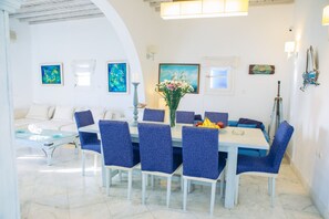 A dining area with a white table and blue chairs, surrounded by white walls and artwork. - Mykonian style house ,3 min walk from Ornos Beach (Ornos)