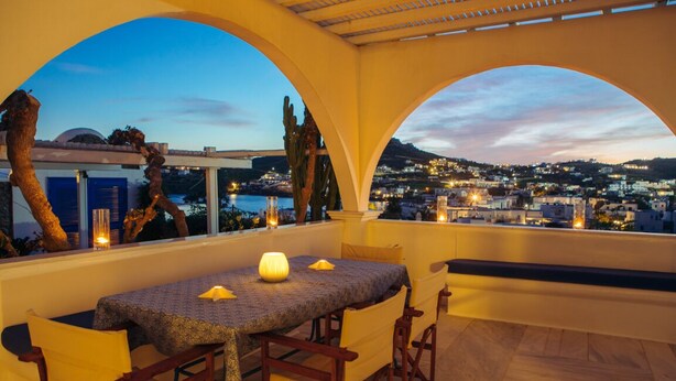 Terraço com mesa e cadeiras, com vista para a paisagem urbana ao entardecer.