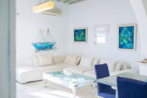 A modern living room with a white sofa, a glass coffee table, and a blue chair. There are paintings on the wall and a ship decoration. - Mykonian style house ,3 min walk from Ornos Beach (Ornos)