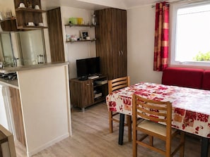 A compact kitchen with a built-in stove, a TV, and wooden cabinets. There's a dining area with a table covered in a floral tablecloth and two chairs. - Mobile home 6 persons air-conditioned- la pignade - Ronce les bains (La Tremblade)