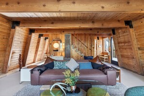 Ein gemütliches Loft-Zimmer mit einem braunen Ledersofa, einem Glastisch und einer Holzbalkendecke.