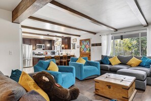 Ein Wohnzimmer mit einer Couch, Sesseln, einer Holzbank und einer Küche im Hintergrund.