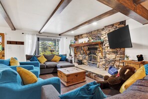 Ein Wohnzimmer mit Kamin aus Stein, einem Flachbildfernseher und einem großen Fenster.