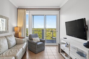 Ein Zimmer mit einer Couch, einem Sessel, einem Fernseher und einem Balkon mit Aussicht.