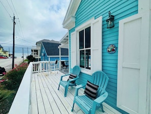 A blue house with a porch, two chairs, and a small sign. - Sandy Toes Stay Coastal 2BDR (Galveston)
