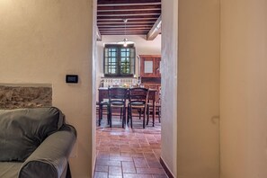 A narrow hallway leading to a dining area with a table set for four, wooden chairs, and a window with a view. - HYDROMASSAGE BATHTUB-AGRITURISMO FATTORIA LA PIEVE-COTTAGE OLIVO 8 km from Pisa (calci)