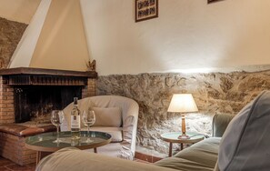 A cozy living room with a stone wall, a fireplace, a sofa, a table with glasses, and a lamp. - HYDROMASSAGE BATHTUB-AGRITURISMO FATTORIA LA PIEVE-COTTAGE OLIVO 8 km from Pisa (calci)