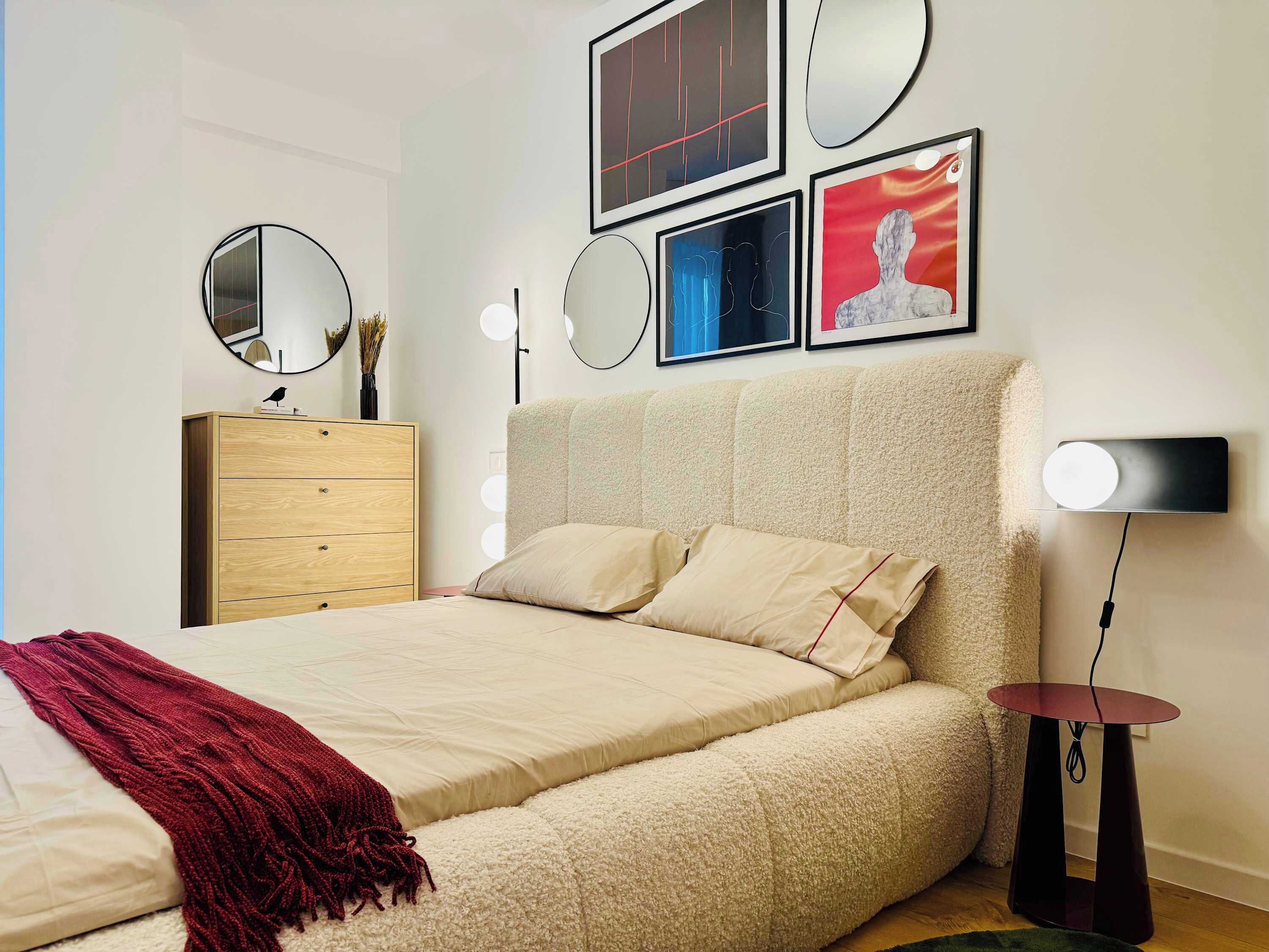 A bedroom with a bed, a dresser, a mirror, and wall-mounted lights.