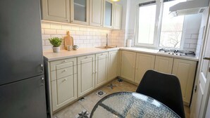 A kitchen with light-colored cabinets, a countertop, a glass table, and a window with an air conditioner. - Joy City Stay Pavel Rotariu 19 (Timișoara)