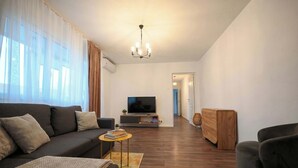 A modern living room with a sofa, TV, wooden cabinet, and a chandelier. - Joy City Stay Pavel Rotariu 19 (Timișoara)