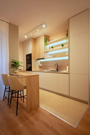 A modern kitchen with a wooden countertop, two bar stools, a black faucet, and built-in appliances. - Joy City Stay | City of Mara M11-61 (Timișoara)